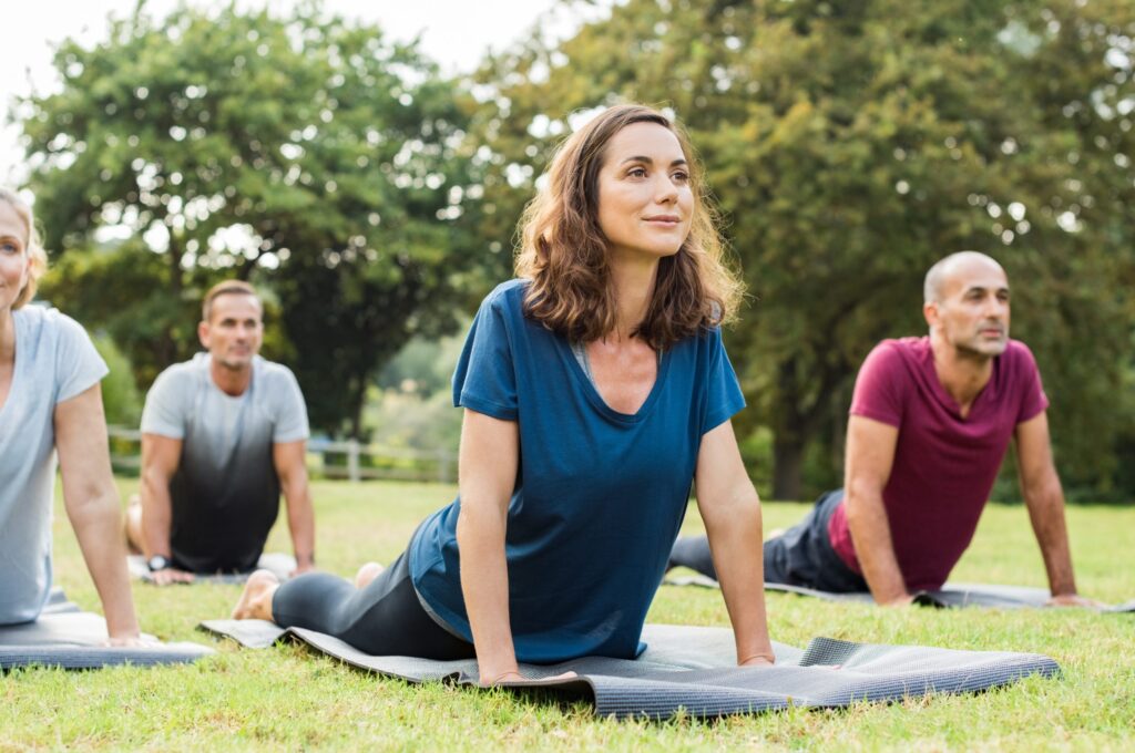 Group of men and women practicing yoga in the park with pleasant looks on their faces.