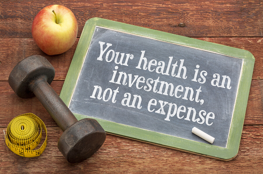 Your health is an investment, not an expense - wellness concept - slate blackboard sign against weathered red painted barn wood with a dumbbell, apple and tape measure